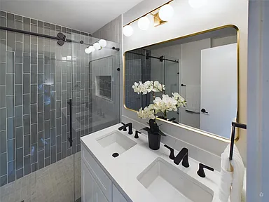 Modern bathroom with glass shower and dual sinks.