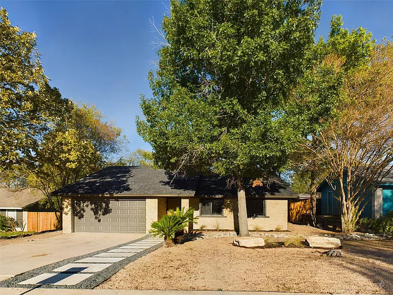 Modern single-story house with a spacious driveway and green trees.