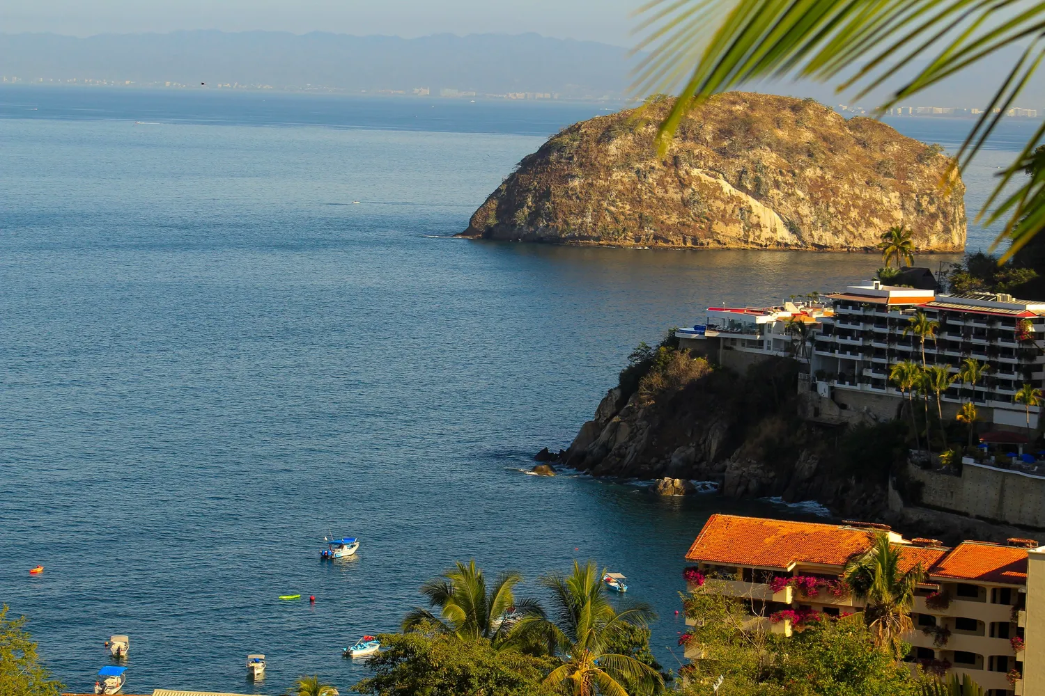 Coastal view with rocky cliffs, calm sea, and boats near the shore.