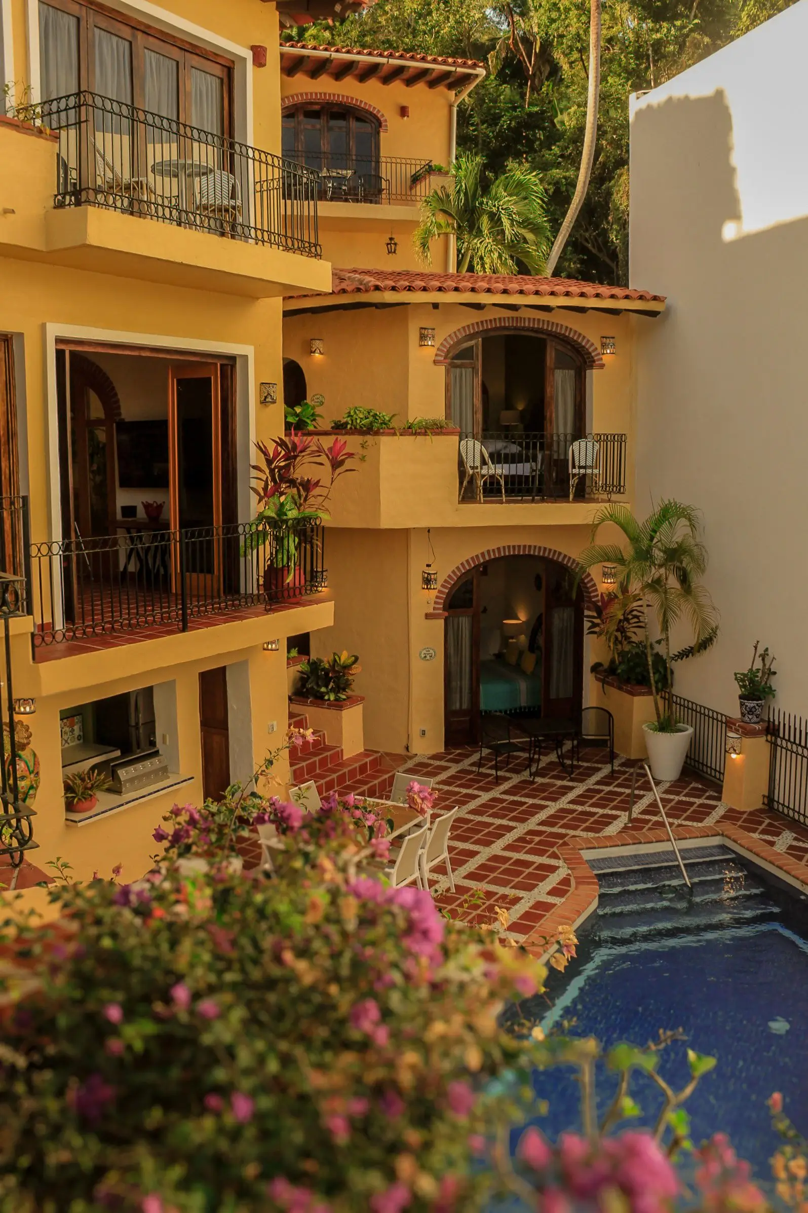 Cozy courtyard with warm lighting and blooming plants around a small pool.